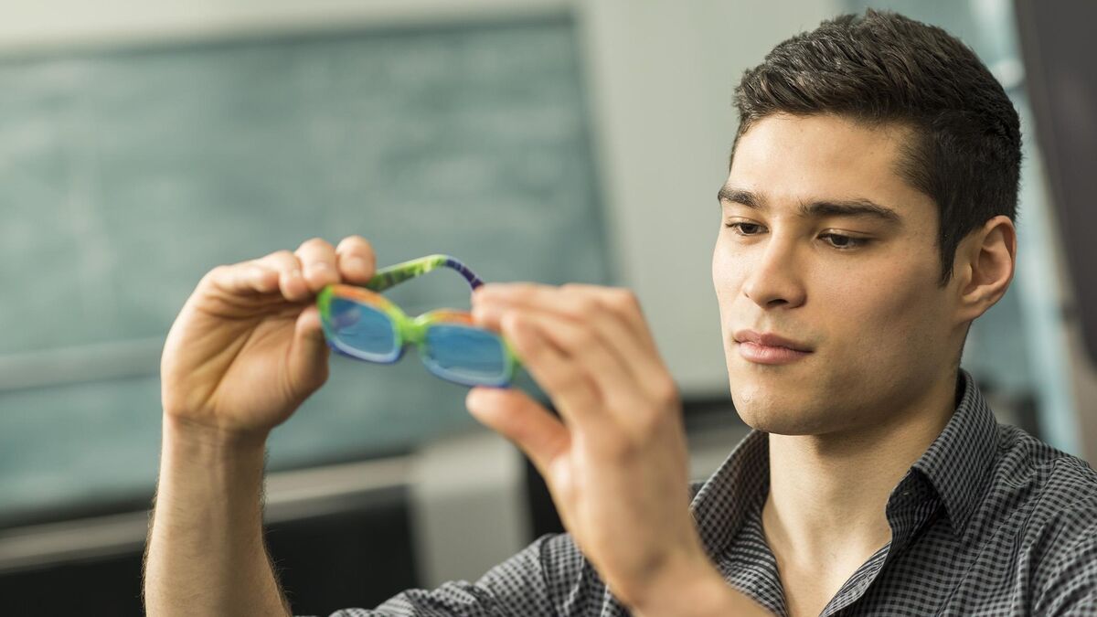 Designer inspecting a green 3D printed sunglasses frame prototype