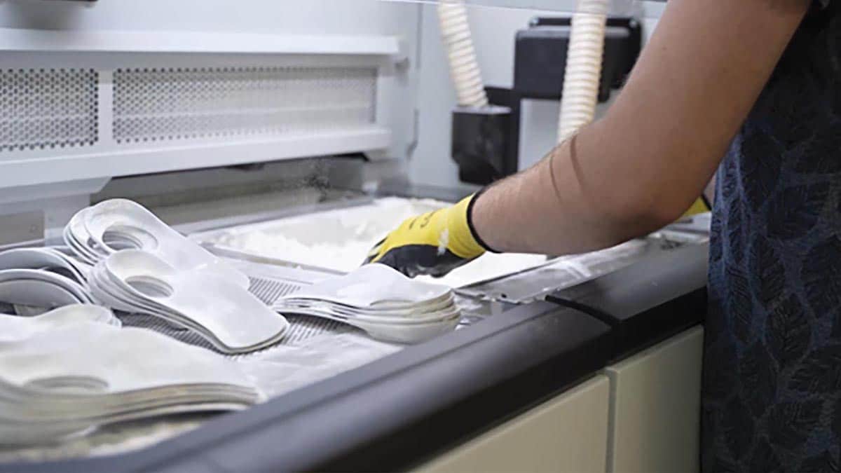 Technician removing 3D printed FitMyFoot custom orthotic inserts from a powder bed printer
