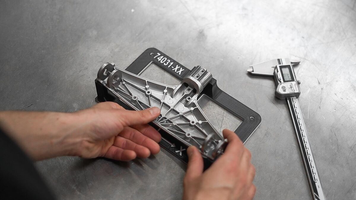 Machinist holding a 3D printed FDM inspection fixture next to digital calipers on a steel surface plate