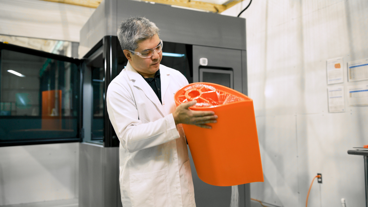 Engineer in a lab coat lifting a large orange SLA part from a Stratasys Neo 3D printer