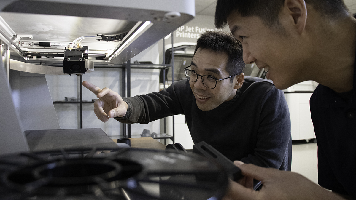 Two engineers examining a spool of filament and a 3D printer part in a print lab