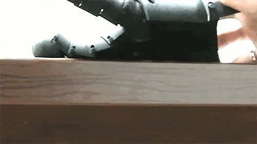 A black 3D printed articulated gauntlet finger from the medieval armor build, captured mid-motion as it flexes like a real knuckle.