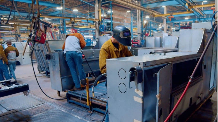Welders in protective gear assembling a row of steel truck service bodies on the Knapheide shop floor