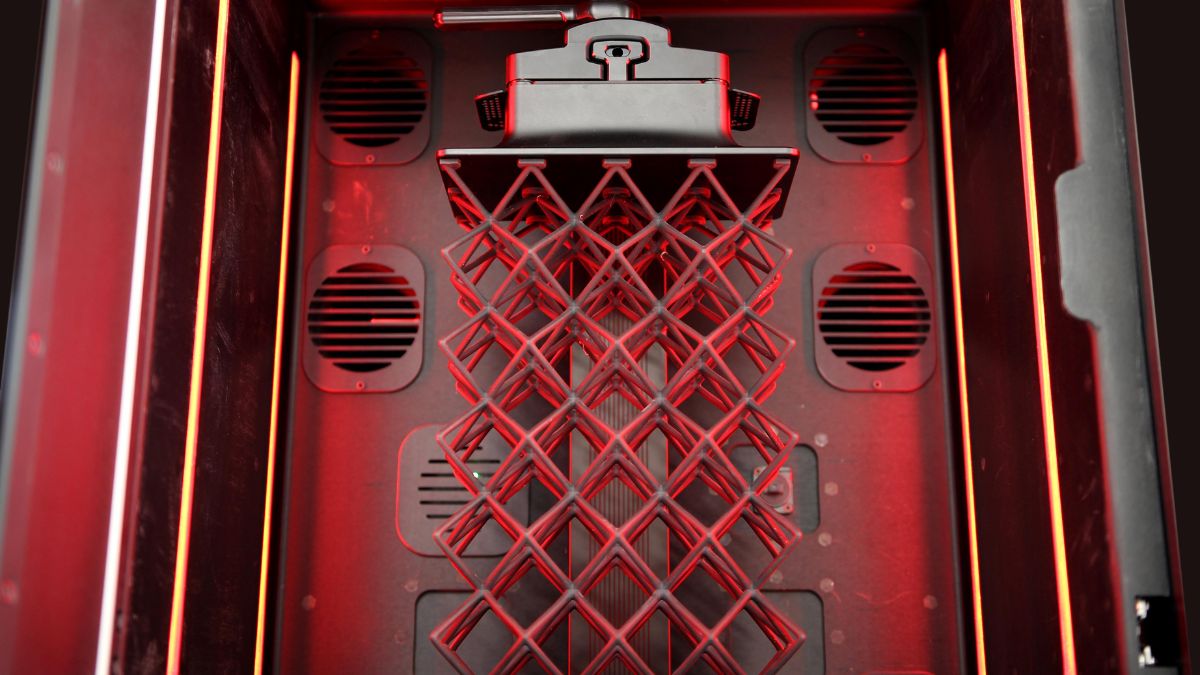 Inside the Stratasys Origin Two printer with a lattice structure suspended under red lighting.
