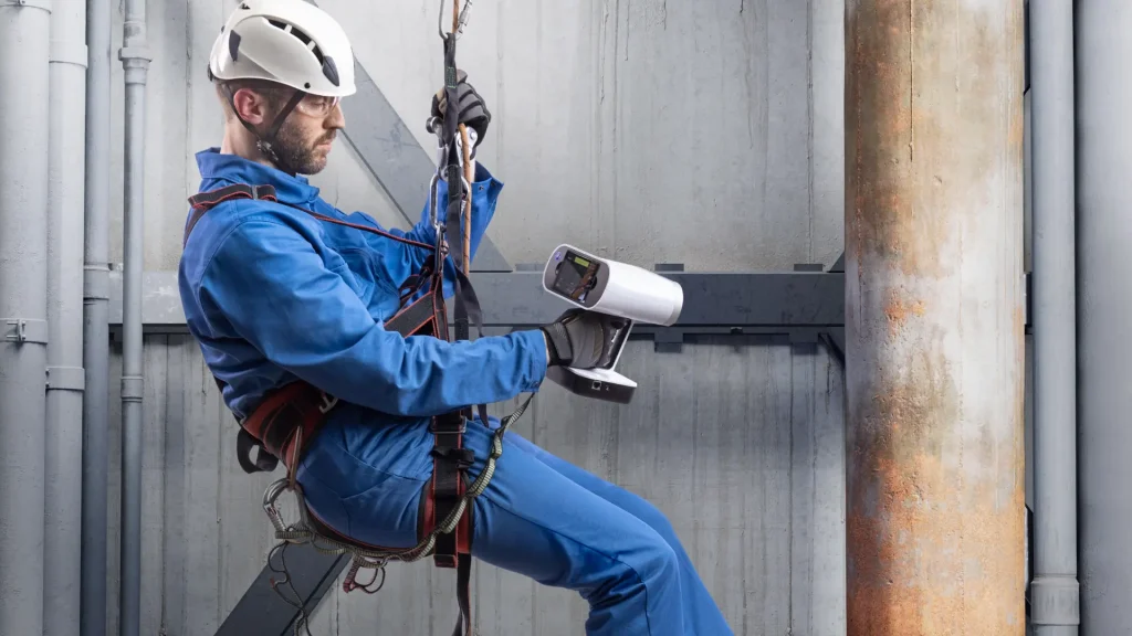 Man climbing down a pipe system with a handheld 3D scanner