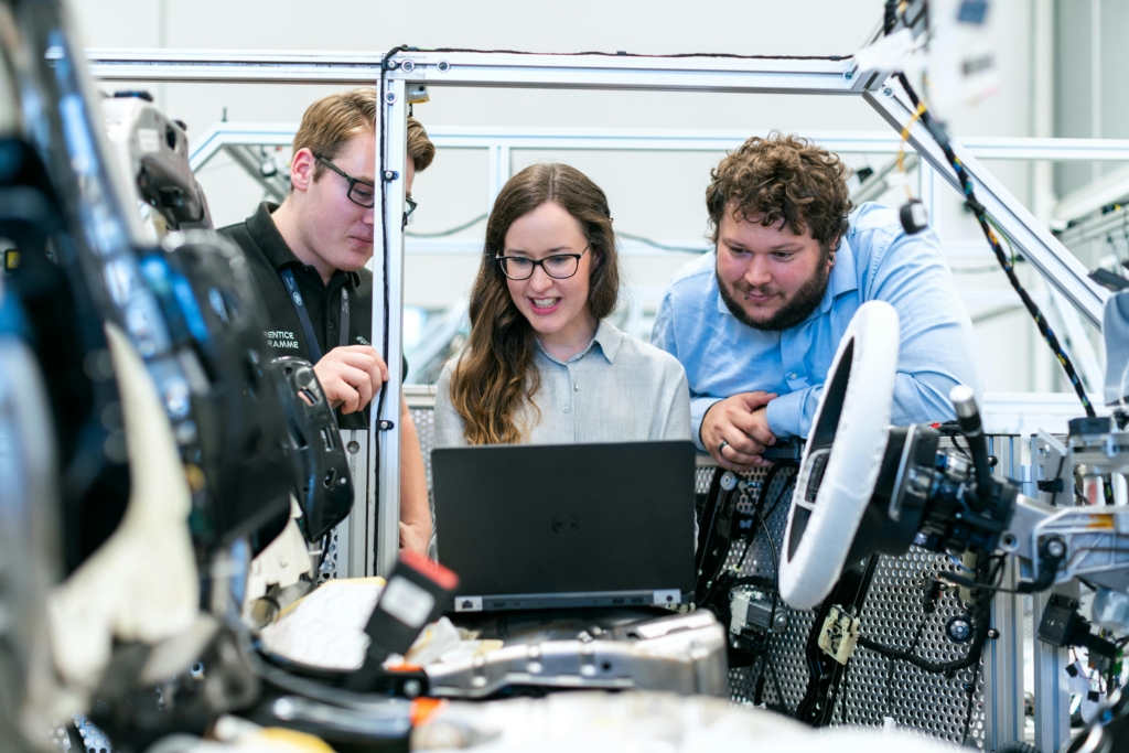 A woman shows two men a car part mock up on her computer screen