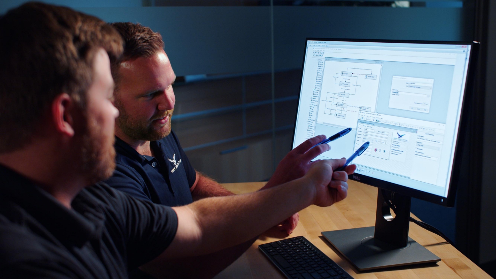 Two engineers reviewing a SOLIDWORKS PDM workflow on a desktop monitor