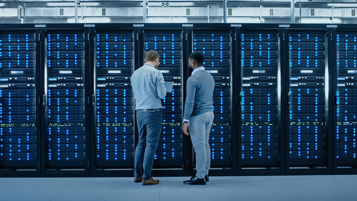 Two IT professionals reviewing rows of blue-lit server racks in a data center